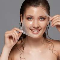 pretty woman with naked shouulders and wet hair removing facial mask isolated on grey, purifiying for face, copy space